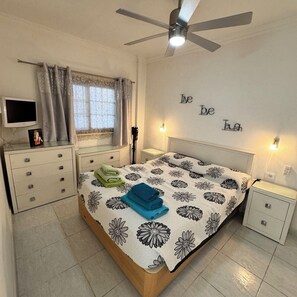 A bedroom with a bed, a ceiling fan, a bedside table, a nightstand, a TV, and a window with curtains. - Relaxation, comfort, and unforgettable views (Costa Adeje)