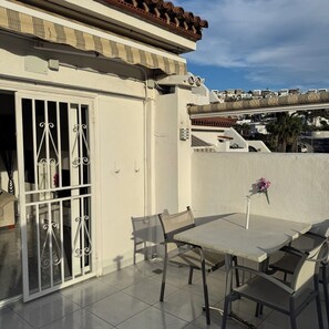 A balcony with a table and chairs, a white door with metal bars, and a view of buildings in the background. - Relaxation, comfort, and unforgettable views (Costa Adeje)