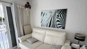 A modern living room with a beige sofa, a zebra print artwork, a hanging macrame light fixture, and a glass door leading to an outdoor area. - Relaxation, comfort, and unforgettable views (Costa Adeje)