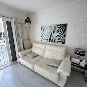 A modern living room with a beige sofa, a zebra print artwork, a hanging macrame light fixture, and a glass door leading to an outdoor area. - Relaxation, comfort, and unforgettable views (Costa Adeje)