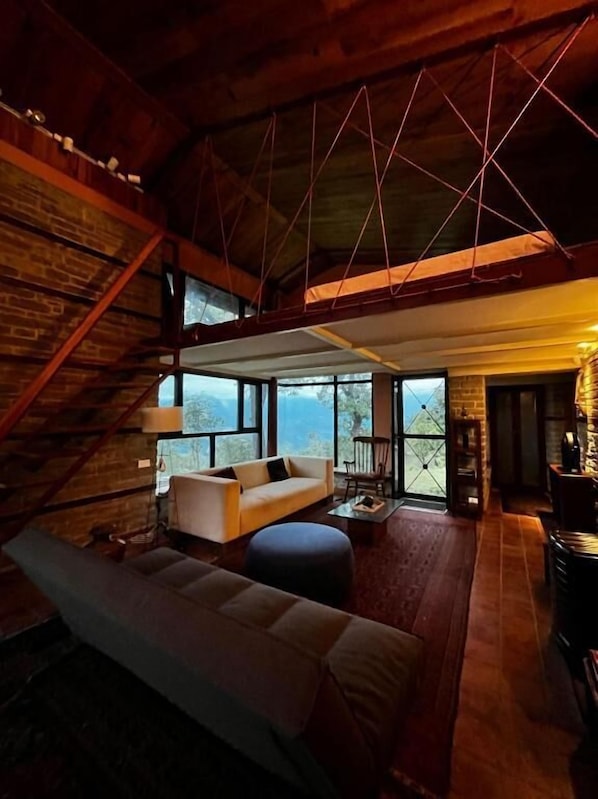 A spacious loft with a high ceiling, a large sofa, a dining table, and a view through the large windows.
