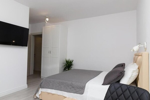 A bedroom with a bed, a TV mounted on the wall, a wardrobe, and a plant.