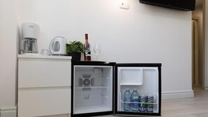 A compact kitchen with a refrigerator, a coffee maker, a kettle, and a wine glass. - Leora Deluxe Apartment  (Split)
