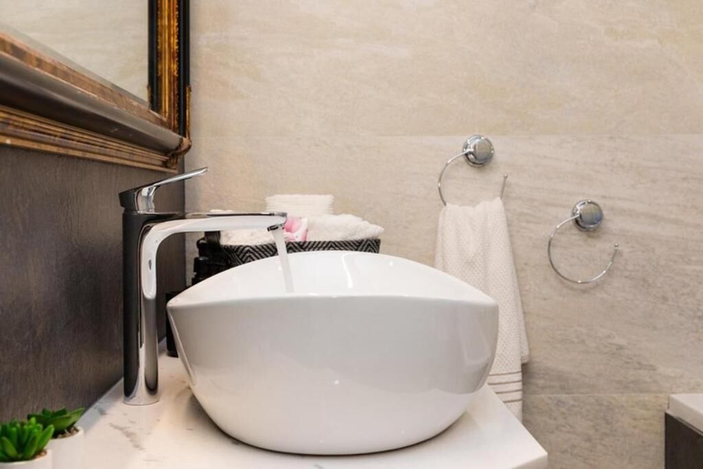 Un baño con lavamanos blanco, un espejo y un perchero para toallas.