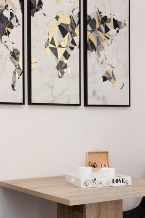 Three framed abstract art pieces on a wall, a wooden table with a tray holding two white cups and a box with the word 'LOVE'. - Leora Deluxe Apartment  (Split)