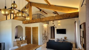 Un vaste espace de vie comprenant une table à manger en bois, un canapé noir et un téléviseur fixé au mur.