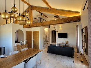 Un vaste espace de vie comprenant une table à manger en bois, un canapé noir et un téléviseur fixé au mur.