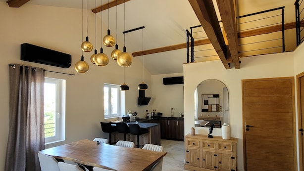 Un grand espace à manger avec une table et des chaises en bois, une cuisine dotée d’un four encastré et un escalier menant à un niveau supérieur.