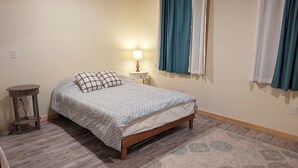 Een slaapkamer met een bed, nachtkastje, lamp en gordijnen.
