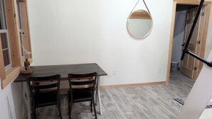 Een eetgedeelte met een houten tafel en stoelen, een hangspiegel en een deur naar een andere kamer.