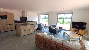 Eine moderne Küche mit Essbereich, ein Wohnzimmer mit Sofa und Fernseher sowie große Fenster.