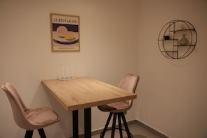Ein kleiner Essbereich mit einem Holztisch, zwei Stühlen, einem Bild an der Wand und einem runden Regal mit Gegenständen.
