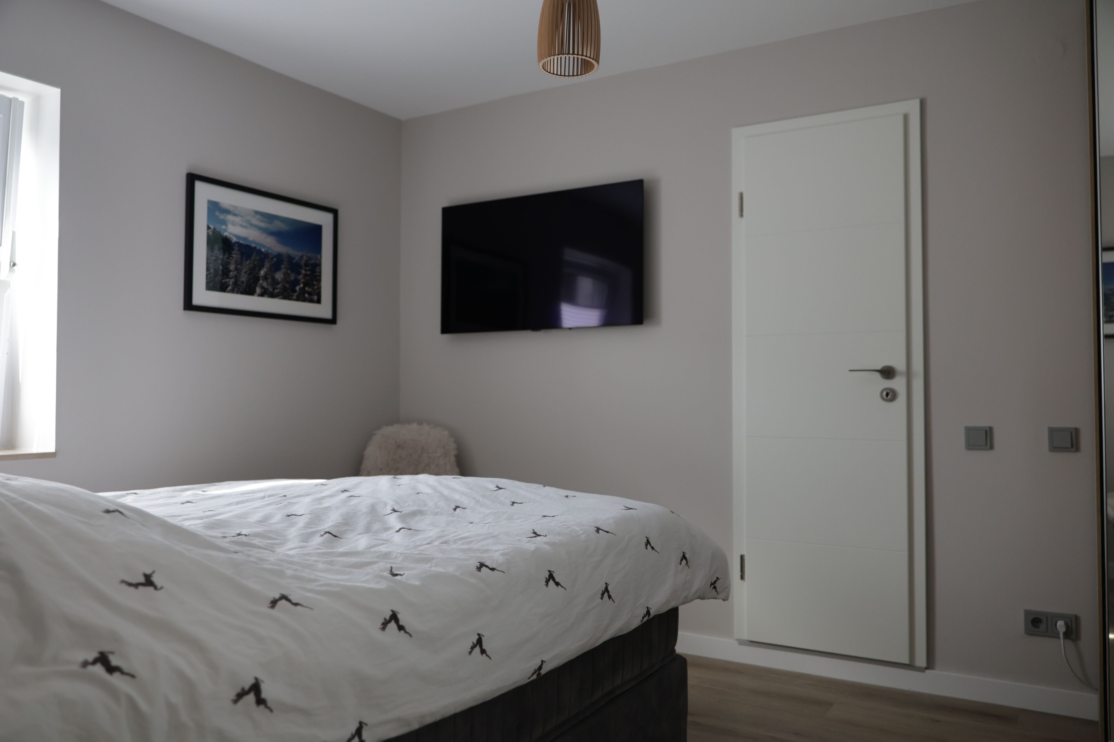 Ein Schlafzimmer mit einem Bett, einem gerahmten Bild an der Wand, einem Fernseher und einer Tür.