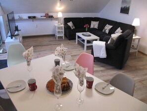 A dining area with a table set for two, a black sofa, and a white radiator in the background. - Sperrental view from the living room (Braunlage)