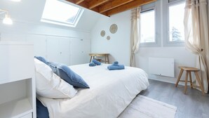 Et soveværelse med seng, ovenlys, træloft, radiator og et vindue med gardiner.
