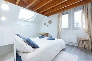 Ein Schlafzimmer mit Bett, Oberlicht, Holzboden, Heizkörper und einem Fenster mit Vorhängen.