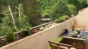 En balkon med et spisebord, omgivet af en betonmur, med udsigt over en skovklædt skråning.