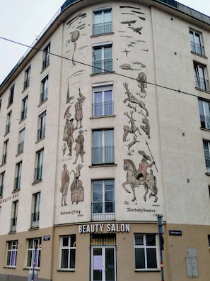 Ein Gebäude mit Wandgemälde von historischen Persönlichkeiten und Tieren, einem Schönheitssalon und einem Schild für 'Ballonaufgieb 1784'.