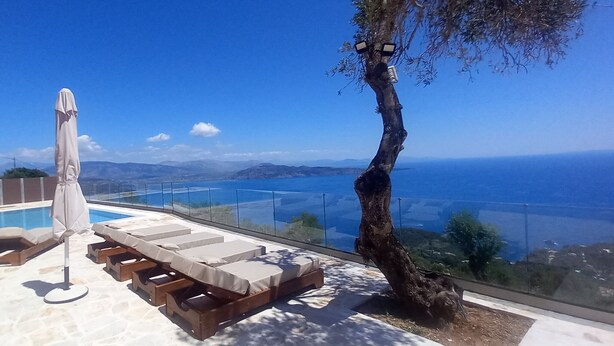 A pool area with lounge chairs and an umbrella, overlooking a scenic view of the sea and mountains. - Stone Villa Vasiliki Private Pool & Sea View (Corfu)