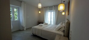 Ein Schlafzimmer mit einem Bett, zwei Pendelleuchten, einem Fenster mit Vorhängen und einem Nachttisch.