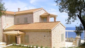 A two-story stone house with a tiled roof, a balcony, and a view of the sea. - Stone Villa Vasiliki Private Pool & Sea View (Corfu)