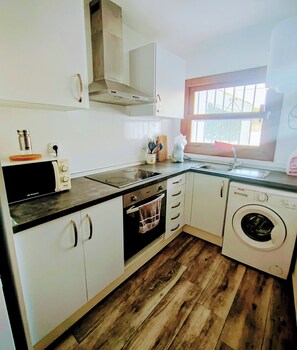 A compact kitchen with a microwave, stove, oven, sink, and washing machine. - House Cala Playa Denia (Denia)