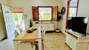 Zona de menjador amb taula, cadires, televisor i finestra que mostra vistes a vegetació.