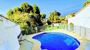 Una piscina amb una terrassa de rajola, envoltada per una paret blanca i una tanca metàl·lica.