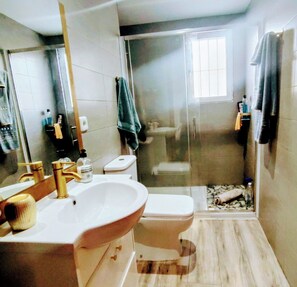 Un baño con lavamanos blanco, grifos dorados, un inodoro y zona de ducha.