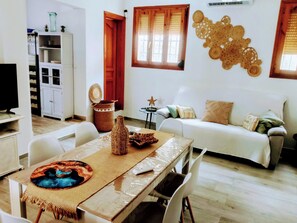 A living area with a sofa, a dining table with chairs, a television, and a kitchen area with cabinets. - House Cala Playa Denia (Denia)