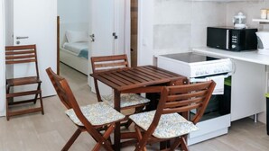 Une cuisine compacte équipée d’une cuisinière, d’un four à micro-ondes et d’un petit four. On y trouve également une table à manger avec des chaises, ainsi qu’un lit dans la pièce adjacente.