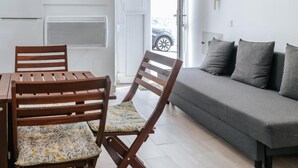 Un espace de vie comprenant un canapé, deux chaises en bois, une table à manger et un coin cuisine avec des placards et un réfrigérateur.