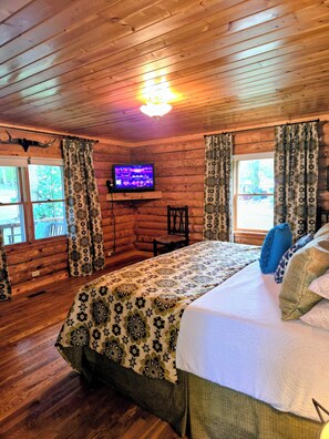 Ein Blockhauszimmer mit einem Bett, einem Fernseher und einem Fenster mit Vorhängen.