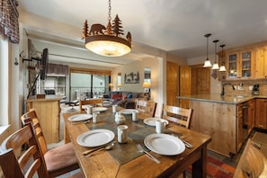 A dining area with a wooden table set for four, a chandelier, and wooden cabinets in the background. - Quiet Walk to Slopes Condo 660 (Mammoth Lakes)