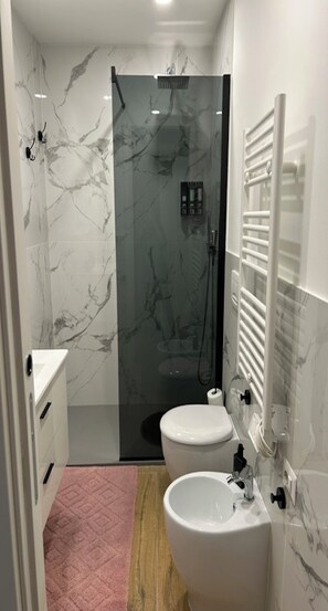 A modern bathroom with a glass shower enclosure, a white toilet, and a sink with a mirror. - MiniHome Turin (Torino)