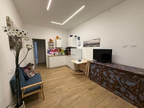 A modern kitchen with white cabinets, a wooden dining table, and a TV on a patterned cabinet. - MiniHome Turin (Torino)