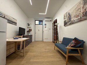A compact living space with a kitchenette, a dining area, a seating area with a sofa, and a door leading to another room. - MiniHome Turin (Torino)