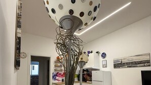 En moderne stue med en usædvanlig kuglelampe, en blå sofa og et køkken i baggrunden.