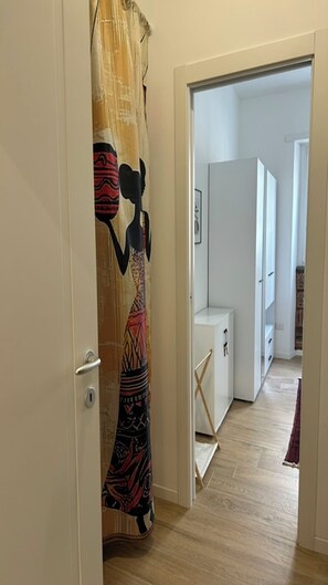 A hallway with a patterned curtain, a white door, and a view into a room with a white cabinet and a framed picture on the wall. - MiniHome Turin (Torino)