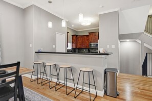 A kitchen with wooden cabinets, a black countertop, and four bar stools. - Modern EaDo Home - Walk to Convention Center, Stadiums & Downtown (Houston)