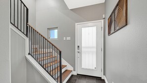 A staircase with wooden steps and black railings, a white door, and a small window. - Modern EaDo Home - Walk to Convention Center, Stadiums & Downtown (Houston)