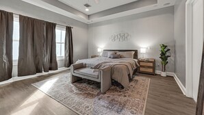 A bedroom with a bed, bedside tables, a ceiling fan, a large window with curtains, and a patterned rug. - Modern EaDo Home - Walk to Convention Center, Stadiums & Downtown (Houston)