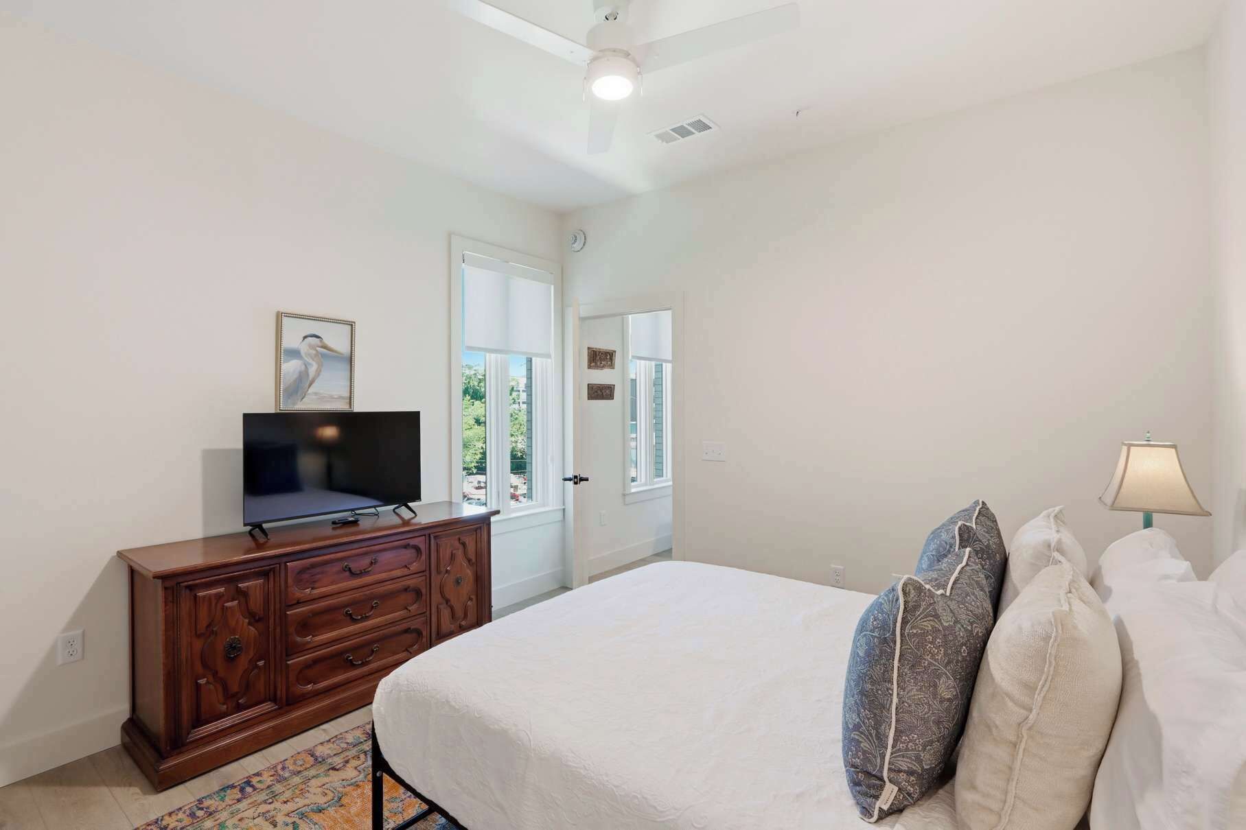 A bedroom with a bed, a dresser, a television, and a window.