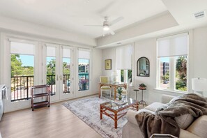 Ein geräumiges Wohnzimmer mit großem Fenster, Deckenventilator und Blick ins Freie.