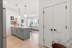A modern kitchen with grey cabinets, a central island, pendant lighting, and a dining area with a sofa and coffee table. - The Gardenia Family Suite | Near Downtown (Savannah)