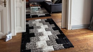 An open doorway leading to a living room with a dark sofa, a patterned rug, and a painting on the wall. - 4-room apartment in Cuxhaven on the dyke (Cuxhaven)