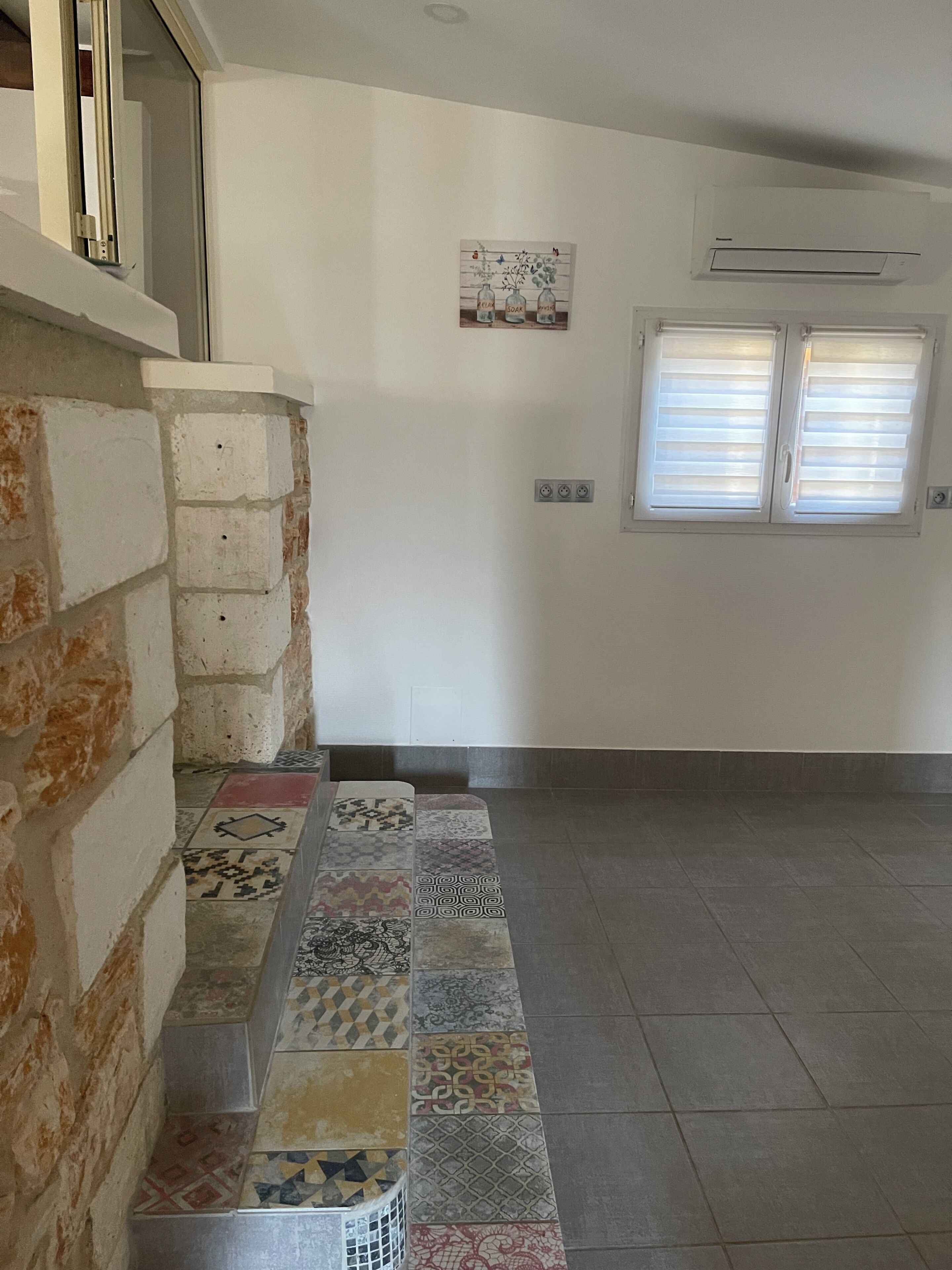A hallway with a patterned tile floor, a brick wall, and a white door.