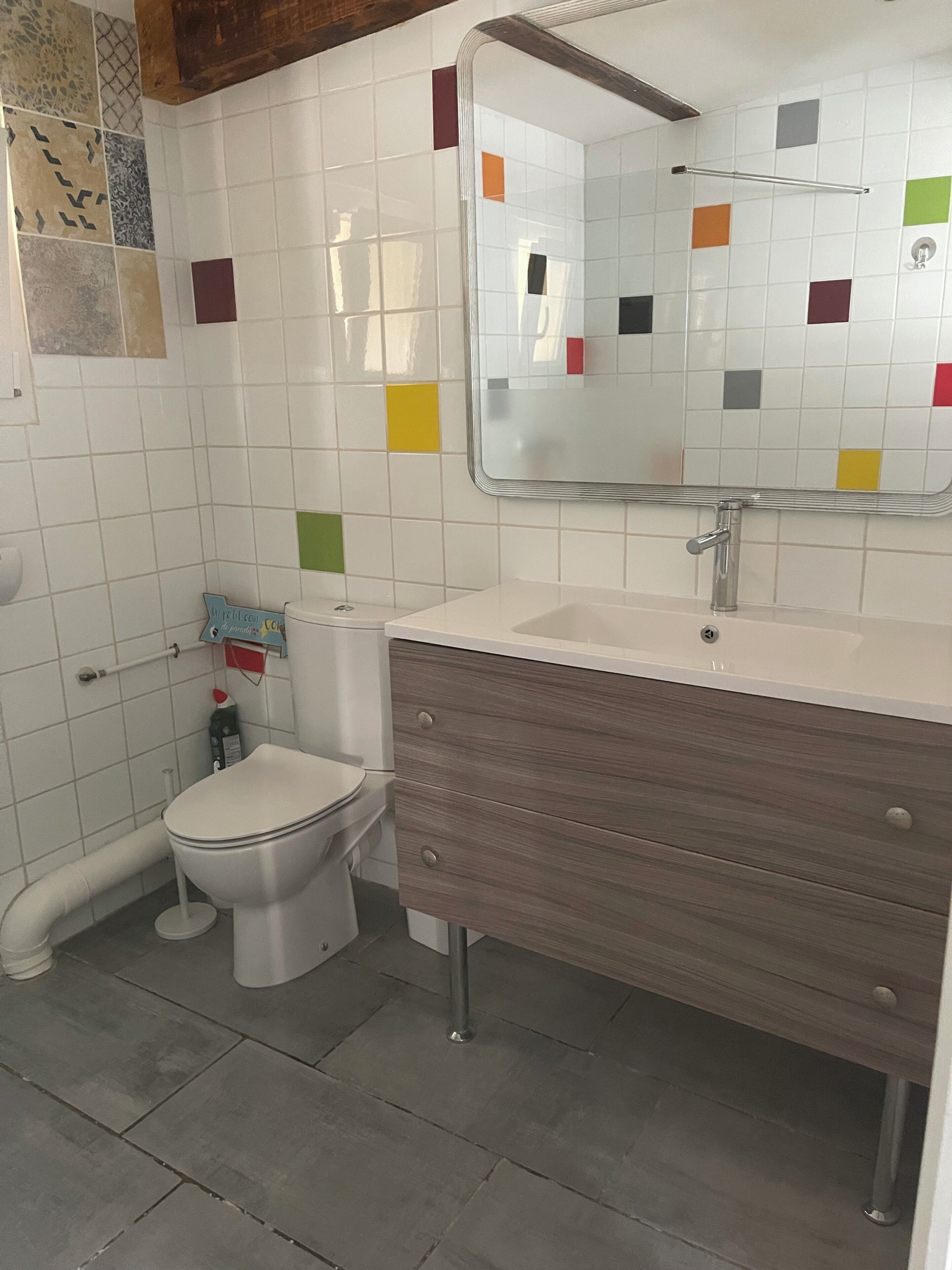 A bathroom with a toilet, sink, mirror, and wooden vanity.