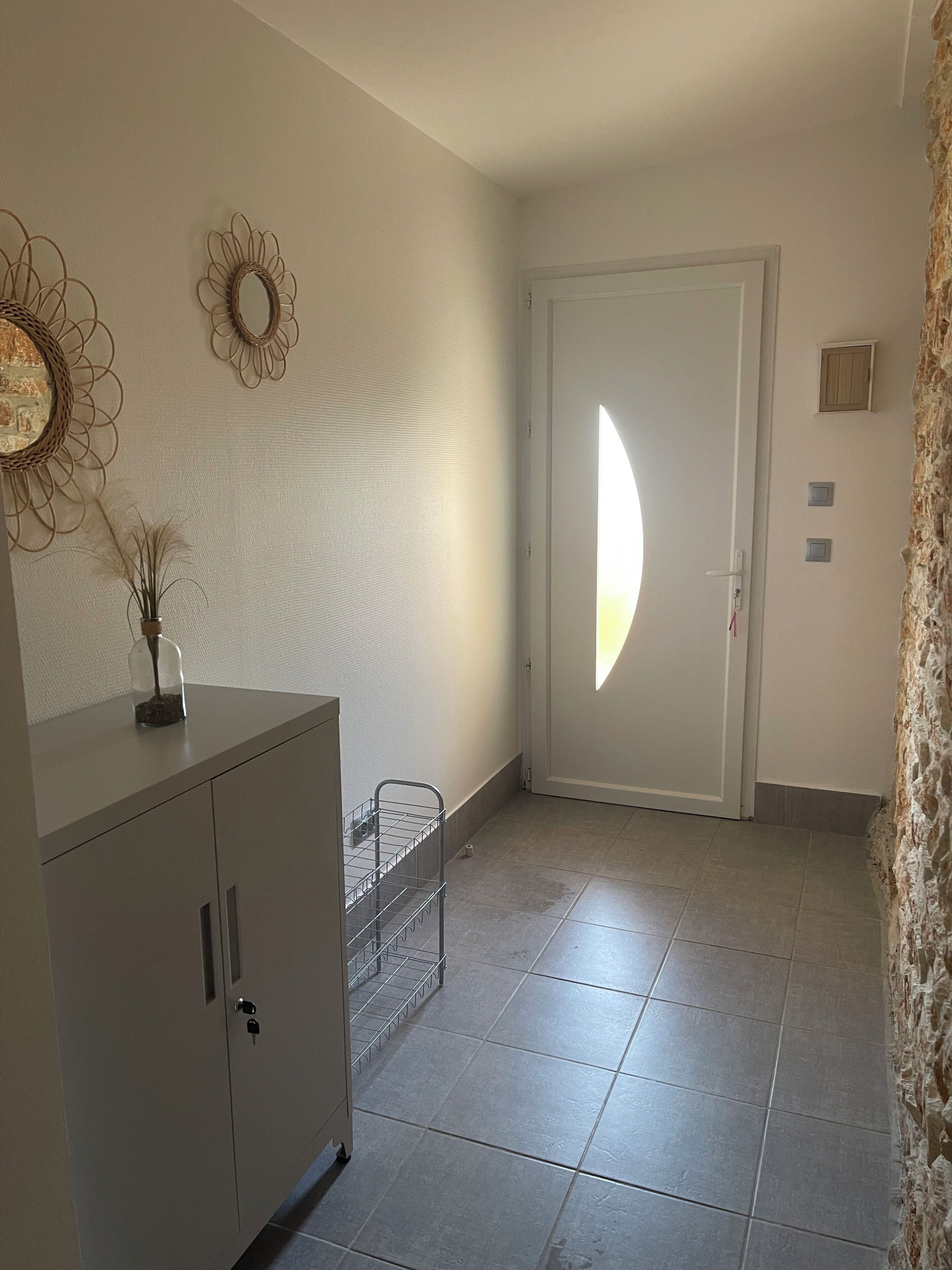 A hallway with a white door, a decorative wall mirror, a metal rack, and a stone wall.