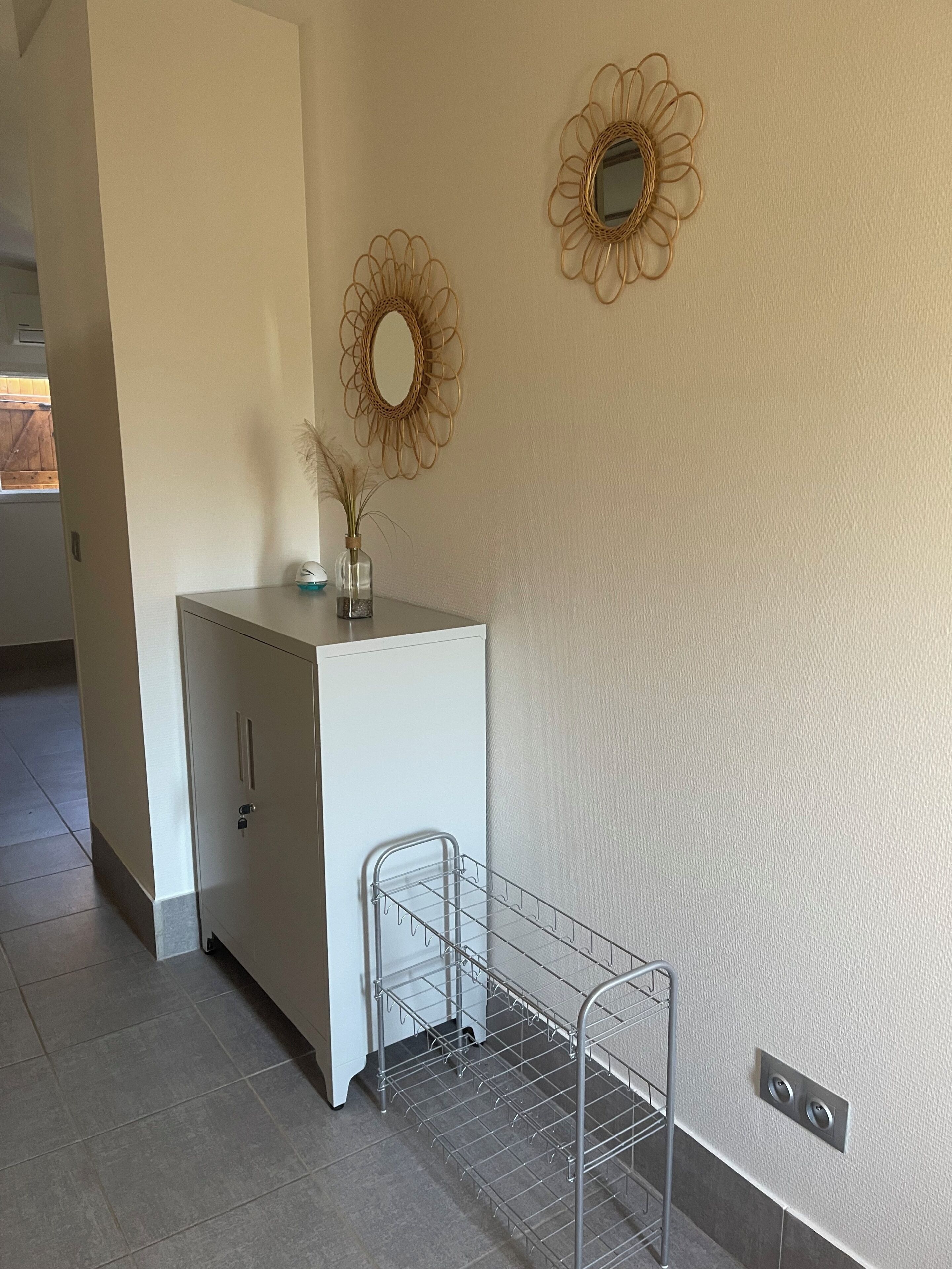 Une pièce comprenant un meuble blanc, une étagère en métal et deux miroirs fixés au mur.